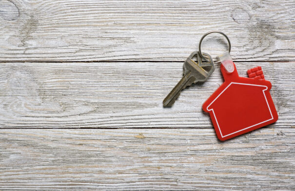 House key on a red color house shaped keychain resting on wooden floorboards concept for real estate, moving home or renting property
